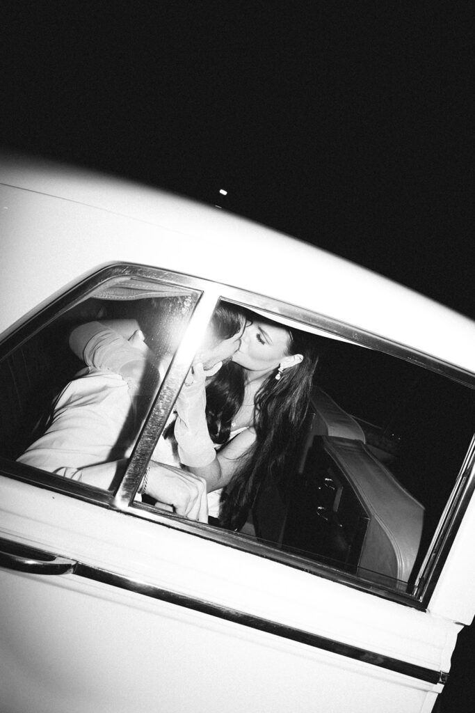 Bride and groom kiss in a classic car in front of The Florentine in Alabama